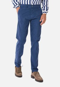 Chino blu navy a gamba stretta, realizzati in cotone con una texture liscia, dotati di una vita classica e tasche laterali, indossati con stivali marroni.