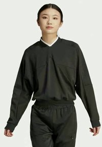 Črni dolg rokav športni top z V-izrezom, ki vsebuje sprednje šive, elastične manšete in sproščen kroj. Narejen iz lahkotne, teksturirane tkanine.