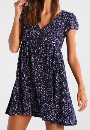 Marineblaues Kleid mit weißen Punkten, kurzen Puffärmeln, V-Ausschnitt und vollem, fließendem Rock mit gerafftem Bund. Weiche Stoffstruktur.