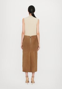 Ärmlös klänning med en beige överdel och en kjol i brun mocka. Har en dragkedja bak, knälång design och en sidoficka. Slät struktur.
