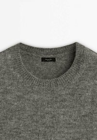 Grå strikket sweater med rund hals og ribbet krave samt et lille sort mærke indeni halsudskæringen.