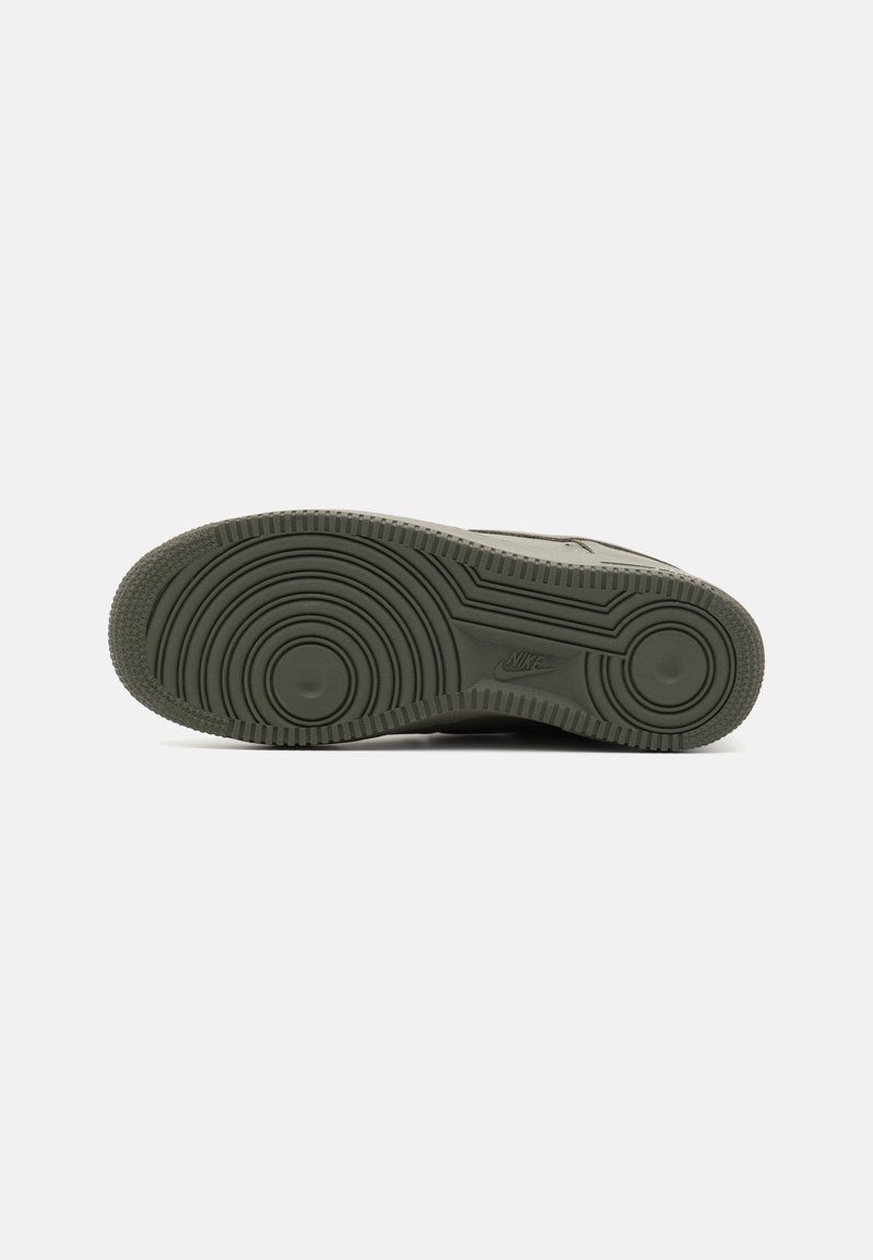 Suela de zapatilla verde oscuro con patrón circular, agarre texturizado y acentos elevados. Presenta el logo grabado cerca de la zona del talón para la marca.