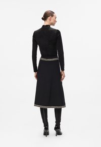 Black long-sleeve top with a textured finish, paired with a black skirt featuring a decorative silver trim at the hem.