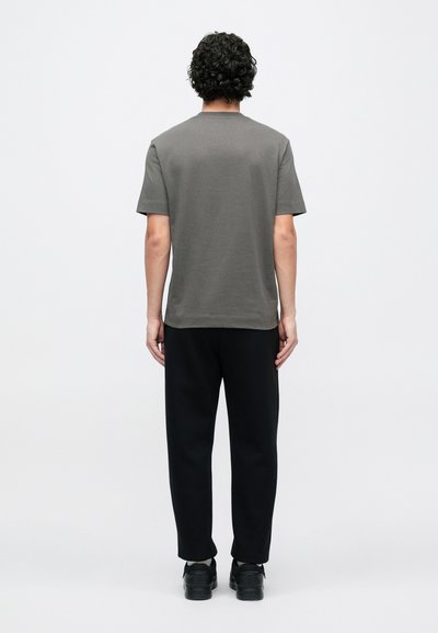 Sivá tričko s krátkym rukávom zobrazené zozadu, v kombinácii s čiernymi nohavicami. Tričko má okrúhly výstrih a jemnú textúru.