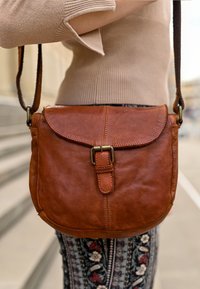 Borsa a tracolla in pelle marrone con forma arrotondata, chiusura a patta e dettaglio con fibbia. La texture è liscia con cuciture visibili.