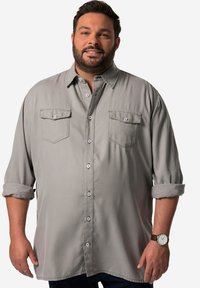 Lichtgrijze langemouwen shirt met twee opgestikte zakken, knoopsluiting aan de voorzijde en opgerolde mouwen. Zachte stof met zilveren knoopaccenten.