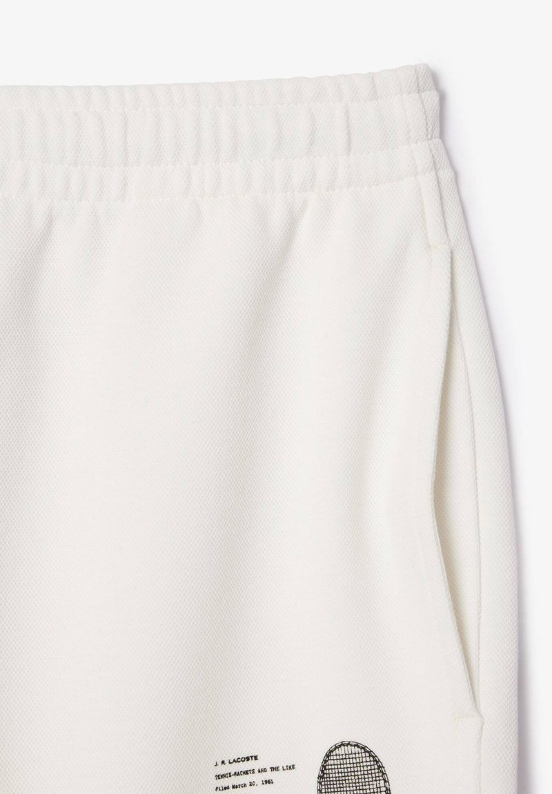 Shorts en tissu texturé blanc avec taille élastique, poche latérale et petit graphique et texte imprimés en noir près de l'ourlet.