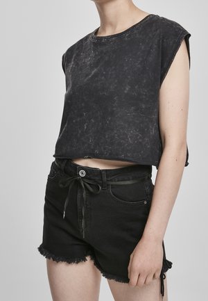 Person iført en falmet sort cropped ærmeløs top og højtaljede sorte denimshorts med frynset kant og et bundet bælte i taljen.