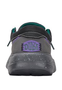 Zapatilla gris con parte superior de malla, detalles en negro y forro verde. Presenta el logo púrpura "HEY DUDE" y una suela gris moteada.