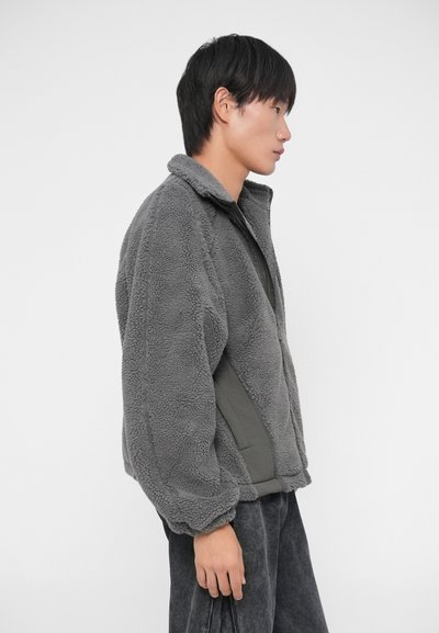 Fleecejacke in Dunkelgrau, mit hohem Kragen und Reißverschluss. Weicher Stoff mit lockerer Passform, versehen mit elastischen Bündchen und Seitenpaneelen.