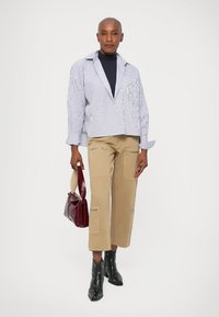 Witte en blauwe gestreepte oversized blouse, beige cropped broek met ritszakken, zwarte enkellaarsjes en een kleine bordeauxrode handtas.
