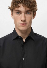 Camisa negra abotonada fabricada con tejido suave, con cuello clásico, tapeta frontal y botones en contraste en los puños.