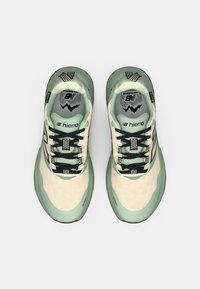 Light cream and mint green athletic shoes with a textured fabric upper, black laces, and a cushioned sole. Features logo and design patterns on the tongue.