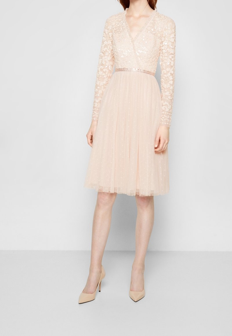 Abito rosa pallido con maniche lunghe in pizzo, scollatura a V profonda e una gonna morbida e plissettata. Presenta dettagli in perline e una cintura in satin in vita.