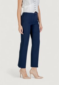 Pantaloni sartoriali blu navy con vestibilità slim, caratterizzati da una texture liscia, passanti per cintura e un design a vita piatta, abbinati a tacchi alti color carne.