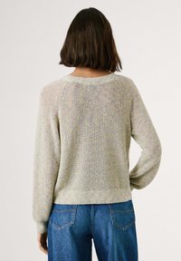 Leicht strukturiertes, pastellfarbiges Sweatshirt mit langen Ärmeln, rundem Halsausschnitt und gerippten Bündchen. Kombiniert mit blauen Jeans.