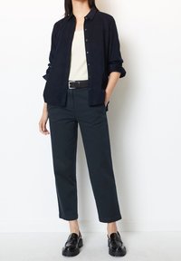 Granatowa koszula na guziki i beżowa koszulka na ramiączkach, zestawione z ciemnymi spodniami. Czarny pasek z metalową klamrą i błyszczące czarne mokasyny. Gładka tkanina, luźny krój.