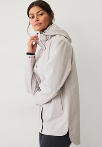 Hellgraue, wasserdichte Jacke mit Kapuze, ausgestattet mit Druckknöpfen, seitlichen Taschen und einem schlanken Design für einen zeitgemäßen Look.