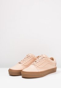 Baskets basses beige avec semelles en caoutchouc marron et lacets, placées côte à côte sur une surface blanche contre un fond blanc uni.