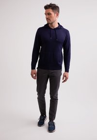 Marinblå huvtröja med känguruficka, strukturerad tyg, kombinerad med slim-fit gråbyxor och blå sneakers med grå detaljer.