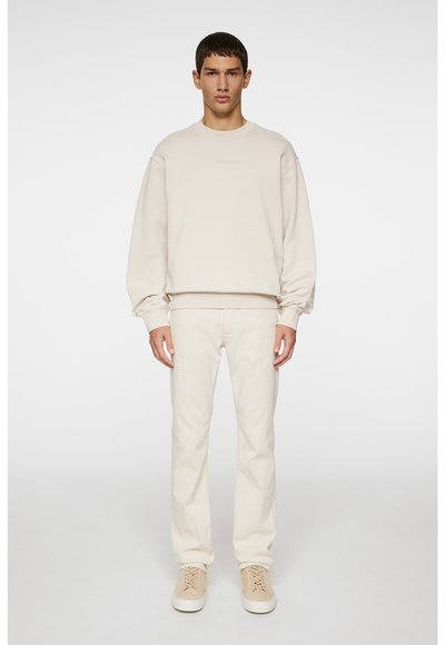 Beige sweatshirt med rund halsudskæring og sænkede skuldre, parret med matchende beige slim-fit jeans og lyse beige sneakers.