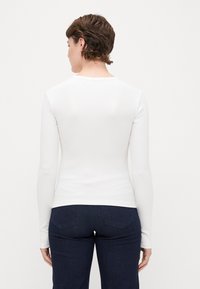 Top branco de malha canelada de mangas compridas com decote redondo. Usado com jeans azul escuro, com bolsos traseiros e um silhueta ajustada.