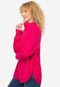 Maglione magenta a collo alto realizzato in materiale morbido, con una vestibilità comoda e spacchi laterali per maggior comfort. Dettagli a coste nei polsini e nel colletto.