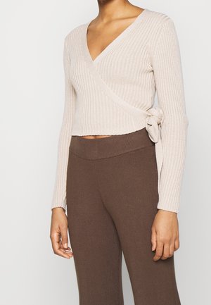 Beige, ribbet indpakningstop med lange ærmer, der har en knytning på siden. Sæt sammen med brune, ribbet, højtaljede bukser.