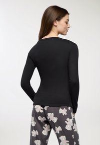 Czarna bluzka z długim rękawem o dopasowanym kroju, gładkiej fakturze i okrągłym dekolcie, w zestawie z szarymi spodniami od piżamy z wzorem misiów.