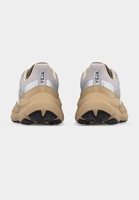 Ζευγάρι μπεζ και γκρι αθλητικά παπούτσια Veja, εμφανιζόμενα από πίσω, με παχιά υφασμένα πέλματα και το όνομα της μάρκας στις γλωττίδες της φτέρνας.