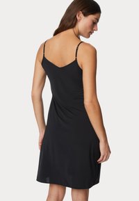 Vestido negro sin mangas con escote en V, confeccionado en una tela suave, con tirantes ajustables y una silueta fluida.