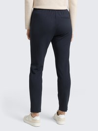 Pantalones de stretch azul marino con cintura elástica, corte ajustado y un bolsillo trasero, combinados con zapatillas color crema.