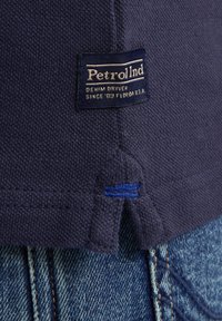 Námořnická modrá bavlněná tričko s texturovaným tkaním. Obsahuje štítek PetrolInd a modrou výšivku na lemu nad džíny.
