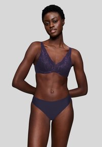 Reggiseno in pizzo di un profondo viola con motivo floreale e spalline larghe, abbinato a mutandine viola solide, caratterizzate da una texture liscia e design senza cuciture.