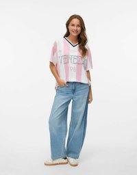 Oversized jersey i pink og hvid strib med "VENEEZA" tekst, rund halsudskæring og afslappet pasform, parret med lyseblå brede jeans og hvide sneakers.