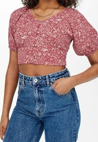 Rote florale zentrale Bluse mit kurzen Puffärmeln und Knopfverschluss, kombiniert mit hoch taillierten hellblauen Jeans aus Denim, die über Fronttaschen verfügen.