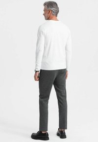 Camicia bianca a maniche lunghe e pantaloni grigio scuro, realizzati in tessuto morbido, abbinati a scarpe nere, visti da dietro.
