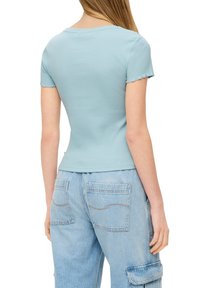 T-shirt azzurro chiaro a costine con maniche corte e una vestibilità leggermente accorciata, abbinato a jeans cargo in denim chiaro con grandi tasche e dettagli di cucitura.