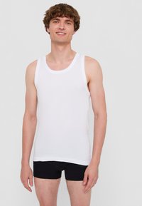 Vit bomullstopp utan ärmar med rund halsringning och breda axelband, tillsammans med svarta boxershorts. Slät textur, avslappnad design.