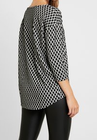 Schwarz-weiß gemusterte Bluse mit Dreiviertelärmeln, die ein geometrisches Design und eine lockere Passform aufweist. Glatte Textur, abgerundeter Saum.