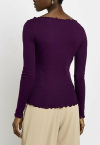 Fioletowy, prążkowany top z długim rękawem, z falbaniastym dekoltem i dołem, o dopasowanym kroju i teksturowanym materiale. Oferuje gładkie wykończenie.