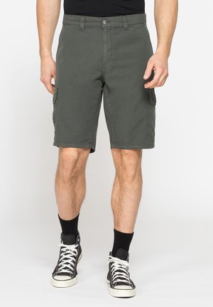 Uomo che indossa pantaloncini cargo grigio scuro, calzini neri e sneakers nere alte, in piedi su uno sfondo semplice.