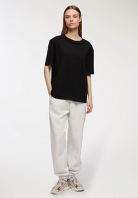 Czarna koszulka z krótkim rękawem o luźnym kroju, w zestawieniu z jasnoszarymi dresami. Beżowe trampki dopełniają całość. Gładkie tekstury materiału.