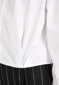 White top with a pleated back, transitioning to black and white striped fabric at the waist. Features a smooth texture and fitted design.