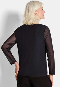 Top nero con maniche lunghe in rete trasparente, scollatura rotonda e corpo interamente nero. Design minimalista senza decorazioni.