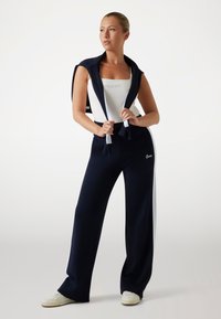 Marineblauw trainingspak met brede broek en aansluitend bovenstuk. Levert witte accenten aan de zijkant en logo-details op de broek. Materiaal van een katoenmix.
