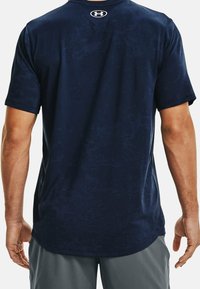 Mörkblå idrottströja med en texturerad mönster, korta ärmar, en böjd fåll och Under Armour-logotyp nära halsringningen.