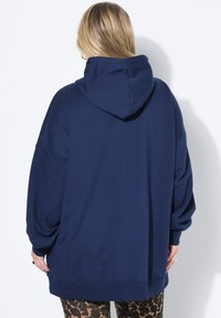 Sudadera holgada de color azul marino con una textura suave, que presenta una gran capucha, hombros caídos y puños acanalados, combinada con leggings estampados.