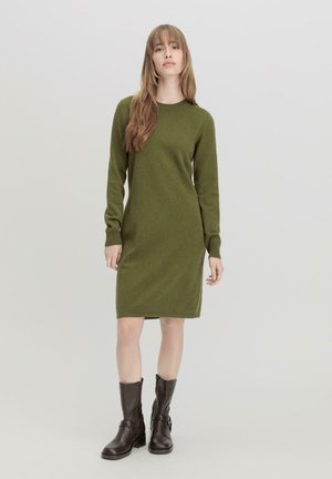 Abito in maglia verde con maniche lunghe, scollo a giro e vestibilità aderente. Abbinato a stivaletti in pelle marrone per un look stratificato.