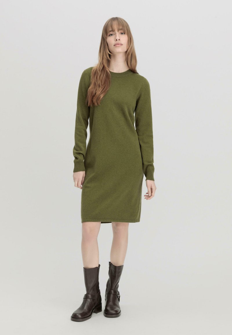 Abito in maglia verde con maniche lunghe, scollo a giro e vestibilità aderente. Abbinato a stivaletti in pelle marrone per un look stratificato.